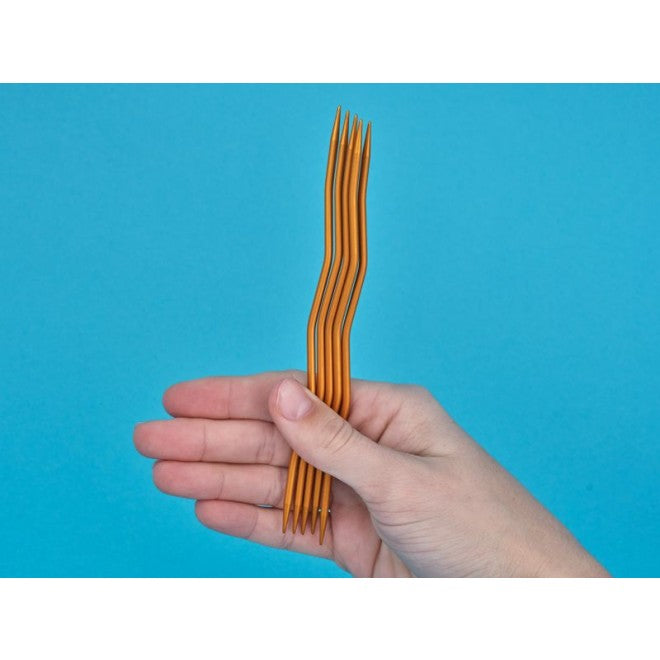 Zwei Hände halten ein kleines Strickstück in Marineblau auf addiCraSySnake-Nadeln — Nahaufnahme zeigt, wie die Maschen auf den welligen Nadeln sitzen.