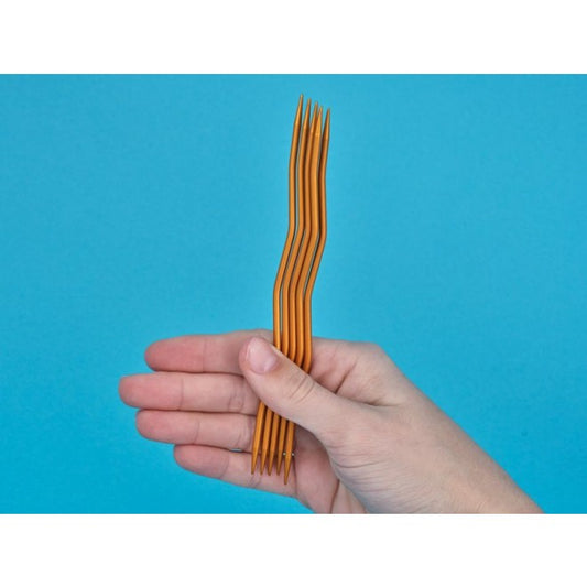 Zwei Hände halten ein kleines Strickstück in Marineblau auf addiCraSySnake-Nadeln — Nahaufnahme zeigt, wie die Maschen auf den welligen Nadeln sitzen.