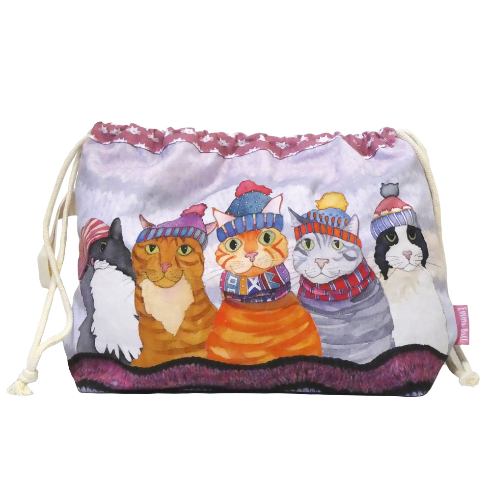 Projektbeutel „Cats in Hats" von Emma Ball auf weißem Hintergrund — Baumwollbeutel mit Kordelzug, bedruckt mit fünf Katzen in bunten Bommelmützen und Schals im Schnee; violett gemustertes Innenfutter am oberen Rand sichtbar.