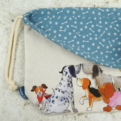 Detailansicht des „Paw Club" Projektbeutels von Eric Heyman. Cremefarbener Stoff mit Aquarell-Illustration: Dalmatiner, Beagle, kleiner Hund mit rotem Halstuch, Spaniel. Innenfutter blau mit Pfoten- und Knochen-Muster.
