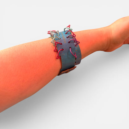 Der Maßgürtel um ein Handgelenk getragen wie ein Armband. In die seitlichen Schlitze sind Maschenmarkierer in Katzenform eingehängt, am Rand läuft die Zentimeter- und Zoll-Skala.