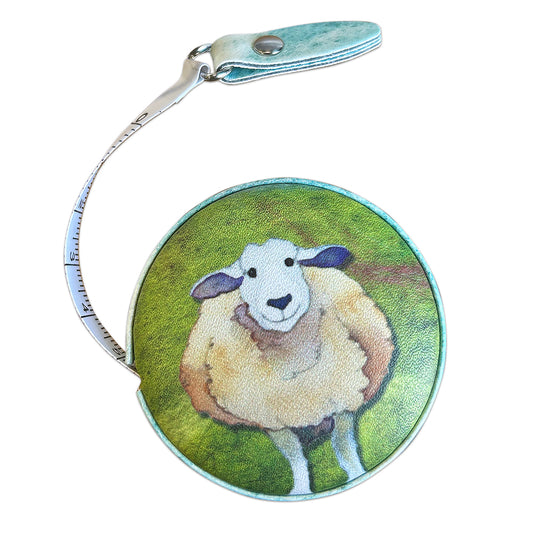 Geöffnetes „Felted Sheep“ Maßband von Emma Ball auf weißem Hintergrund — rundes Gehäuse mit wolligem Schaf auf grünem Hintergrund, teilweise ausgezogenes weißes Maßband und türkisfarbene Lasche mit Druckknopf.