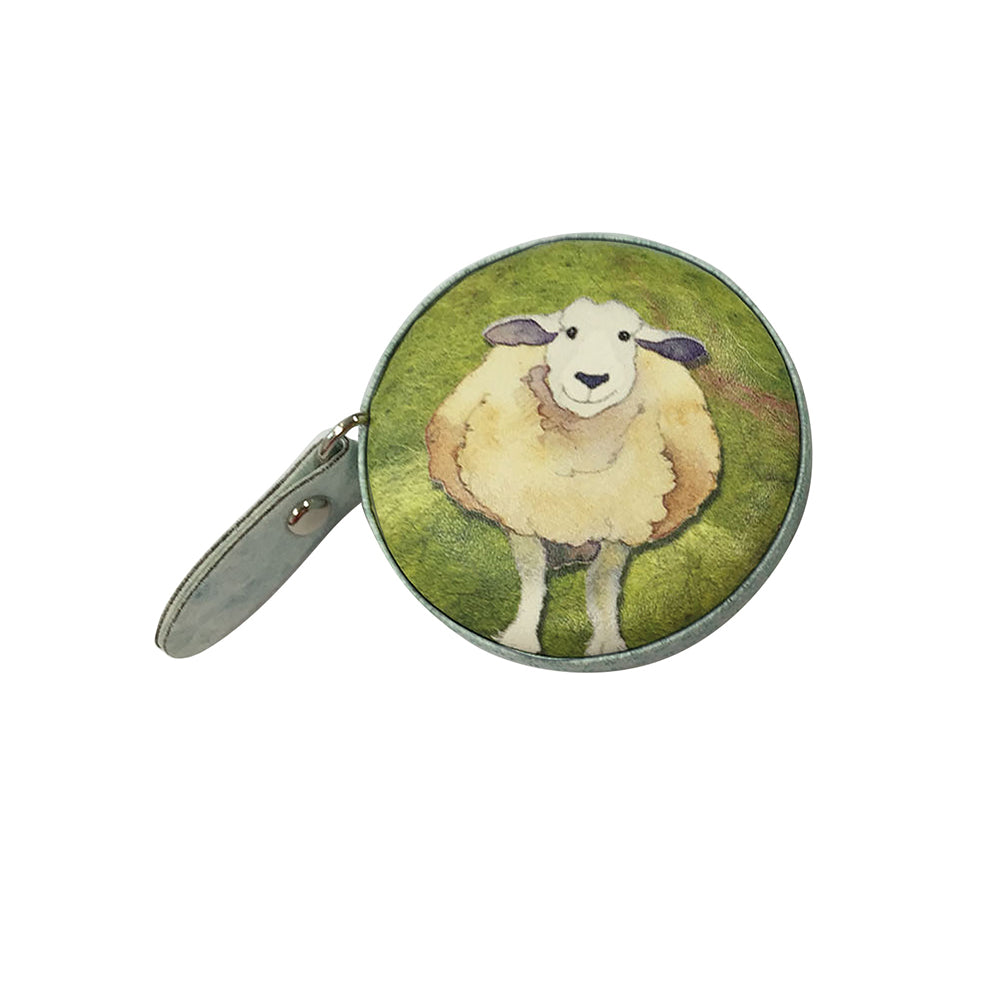 Geschlossenes „Felted Sheep“ Maßband von Emma Ball auf weißem Hintergrund — rundes Gehäuse mit hellem Schaf auf grünem Aquarellhintergrund und seitlicher graugrüner Lasche mit Druckknopf.