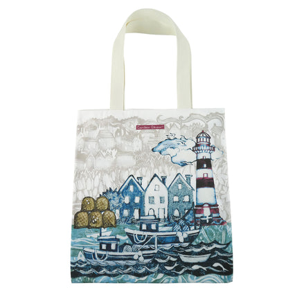 „Fishing Village" Tragetasche von Caroline Cleave auf weißem Hintergrund — großformatige Baumwoll-Canvas-Tasche mit rundum bedruckter Hafenszene: Fischerboote, Häuser, Leuchtturm; cremeweiße Webband-Henkel.